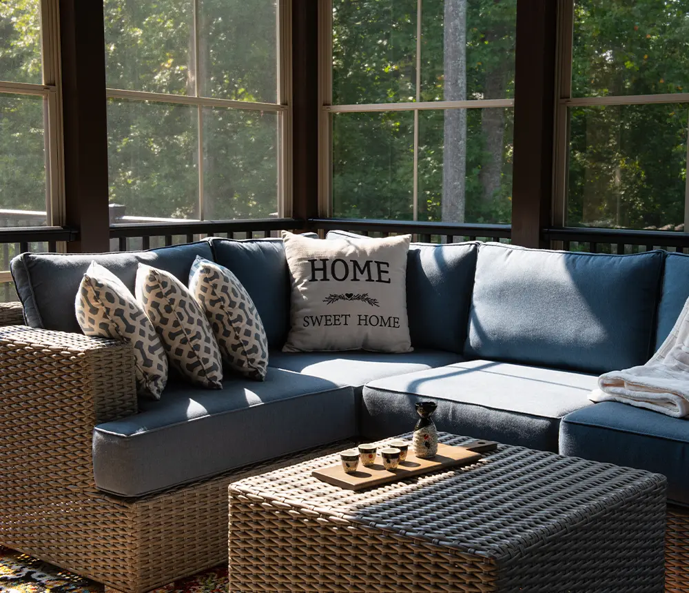 A screened-in porch with an outdoor furniture and pillows that read "home sweet home"