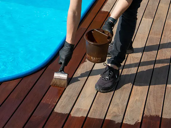 a contractor painting a hardwood deck around a pool