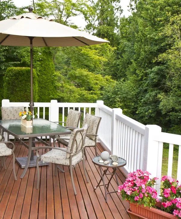 A modern elevated deck featuring white railings, a patio dining table with an umbrella, and vibrant pink flowers, professionally installed by deck building companies in Durham, NC.