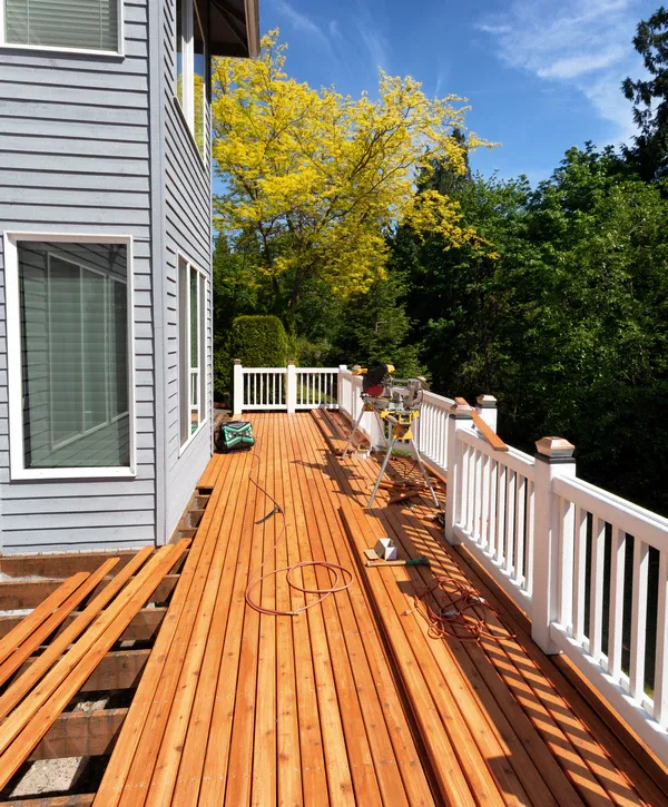 A wide view of a residential deck restoration in progress by deck repair companies in Carrboro, NC featuring new cedar planks and white railings.