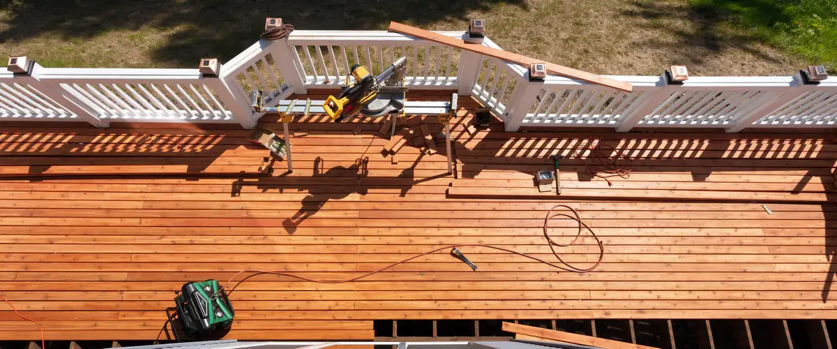 High-angle overhead view of a deck repair project showing a miter saw, air compressor, and newly installed wood boards.