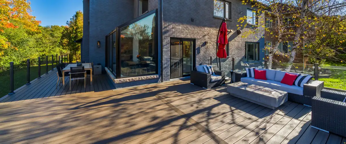 Spacious modern composite deck featuring a large sectional sofa, fire pit table, and dining area overlooking a backyard.